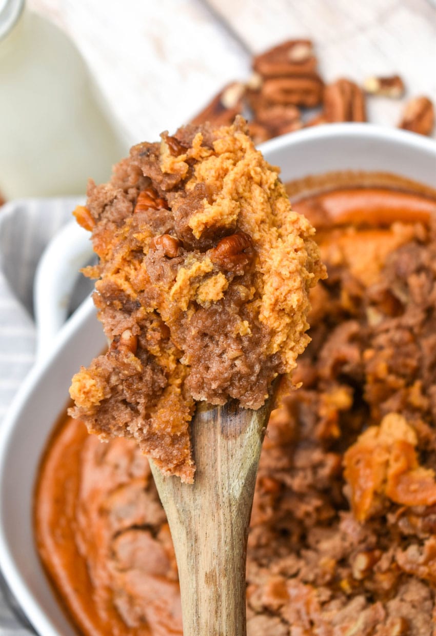 a wooden spoon holding up a scoop of pumpkin pecan dump cake
