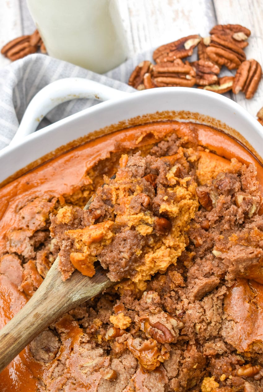 a wooden spoon scooping pumpkin pecan dump cake out of a white casserole dish