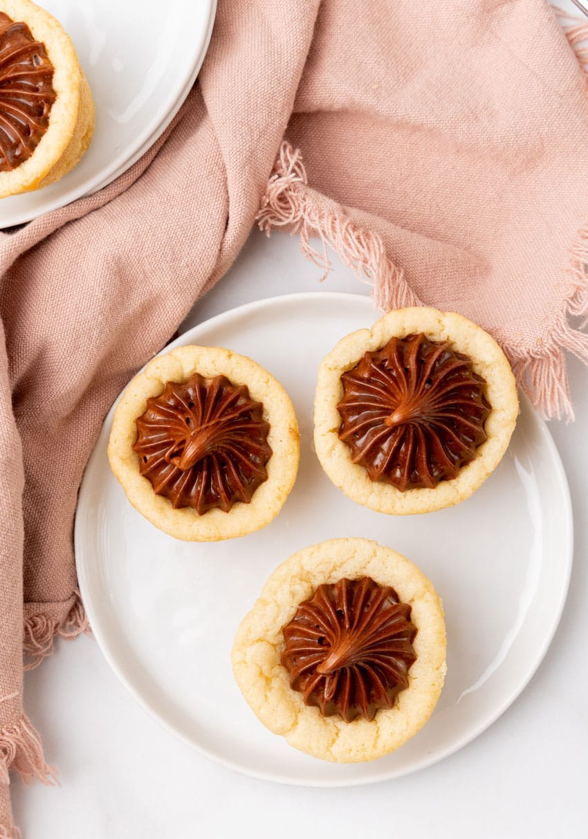three chocolate frosting filled homemade sugar cookie cups on a small white dessert plate