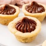 three chocolate frosting filled homemade sugar cookie cups on a small white dessert plate
