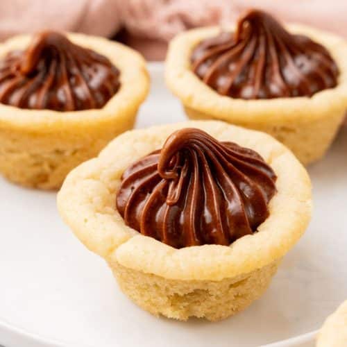 three chocolate frosting filled homemade sugar cookie cups on a small white dessert plate