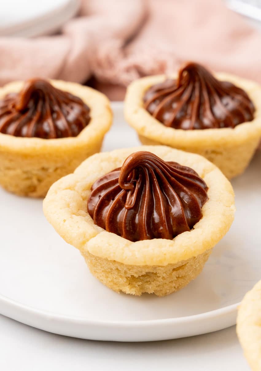 three chocolate frosting filled homemade sugar cookie cups on a small white dessert plate