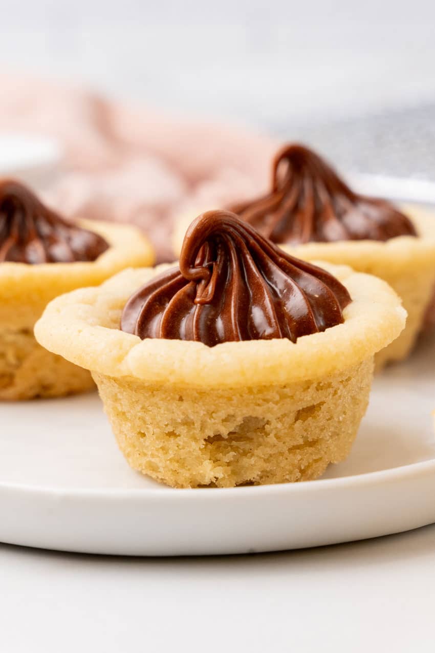 three chocolate frosting filled homemade sugar cookie cups on a small white dessert plate