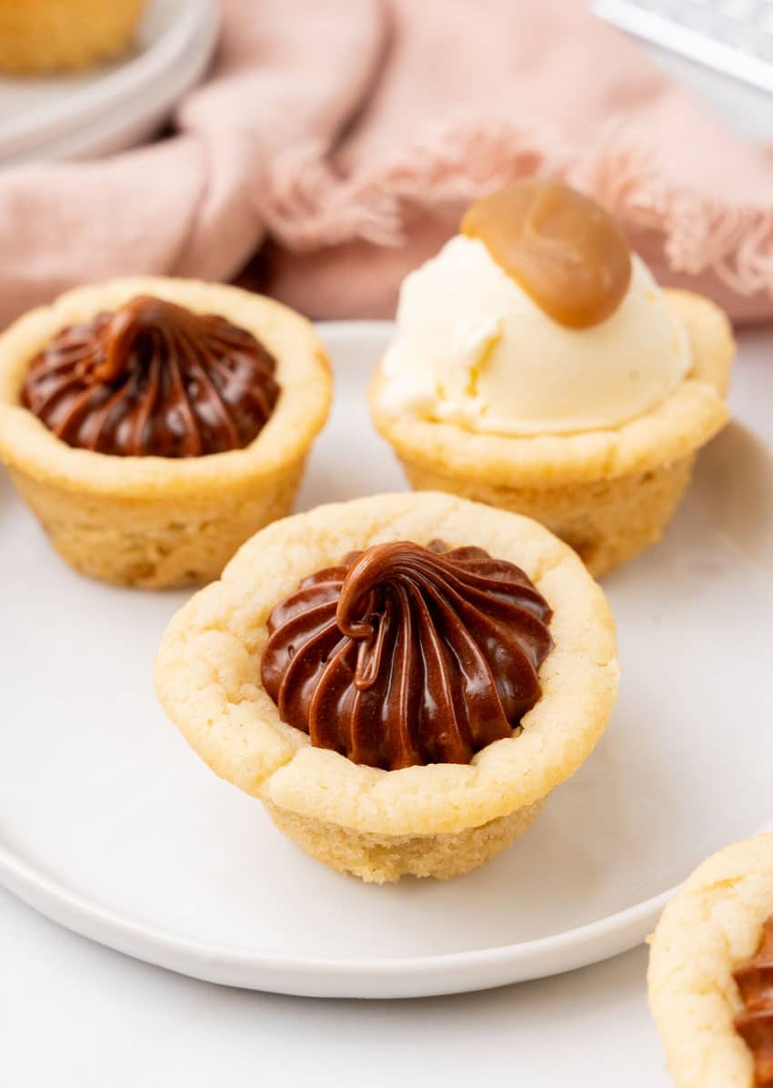three chocolate frosting filled homemade sugar cookie cups on a small white dessert plate