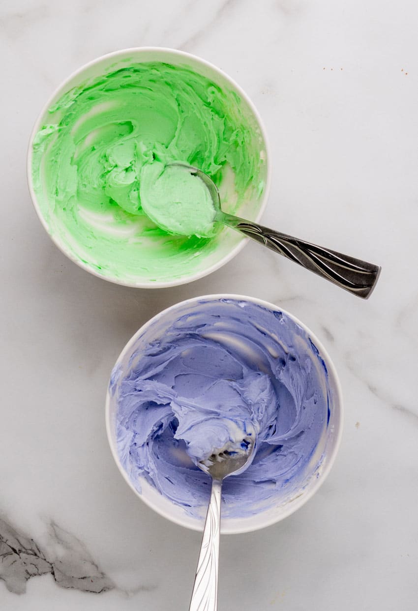 green and purple frosting in two white bowls