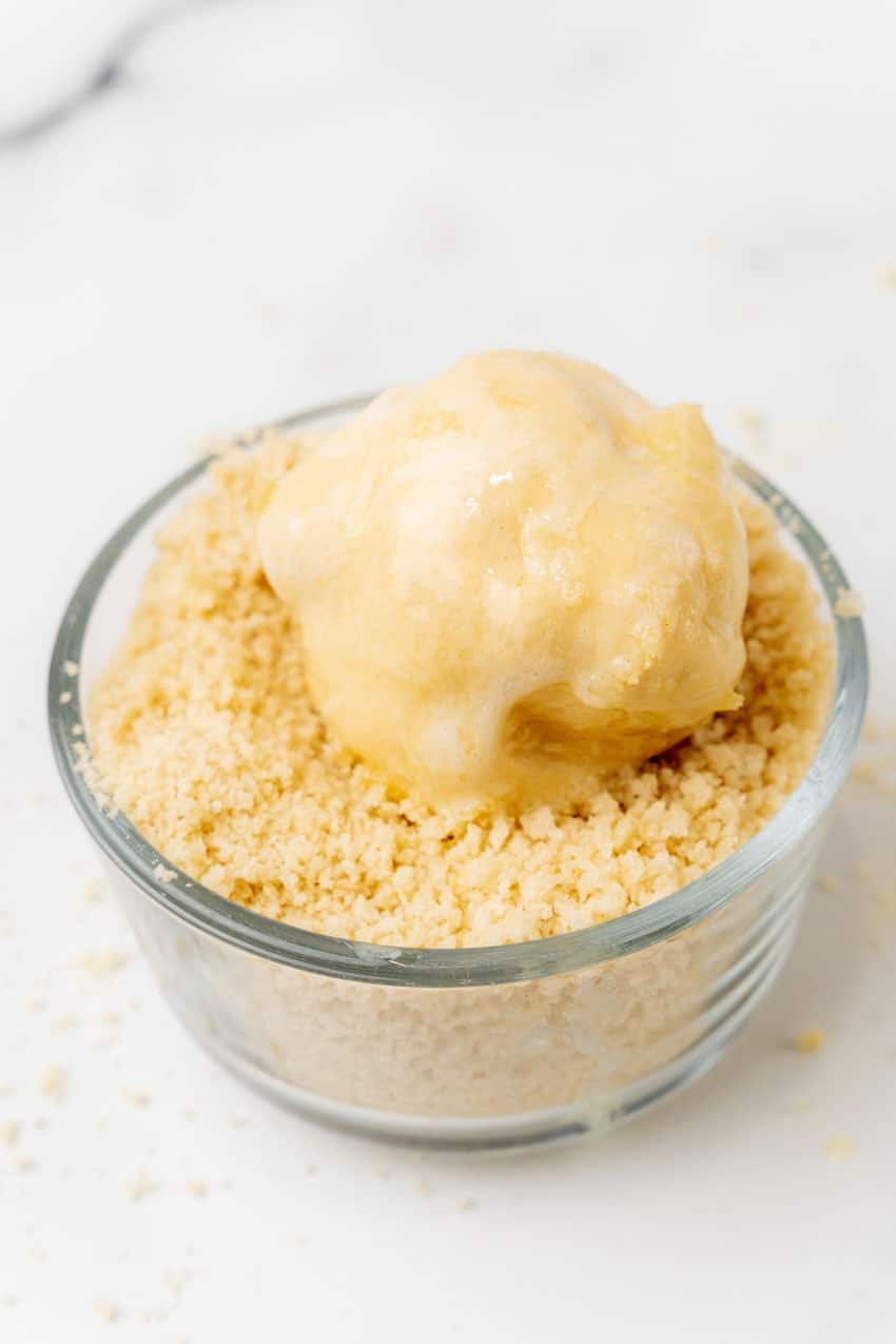 butter coated chicken pillow being rolled in panko bread crumbs in a small glass bowl