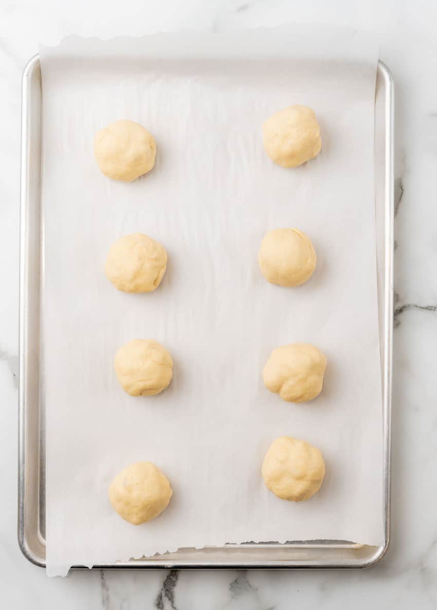 balls of crescent roll dough arranged in two rows on a parchment paper lined baking sheet