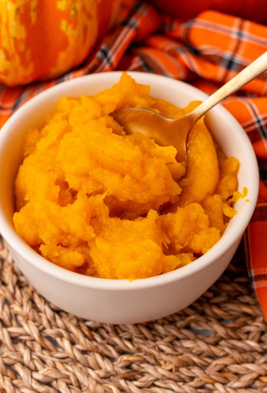 a gold spoon scooping homemade pumpkin puree out of a small white bowl