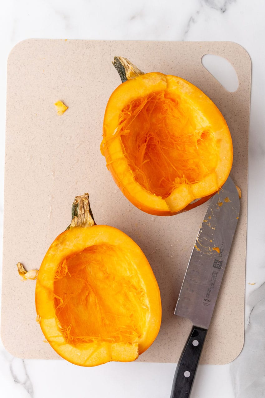two seeded halves of a pie pumpkin on a plastic cutting board