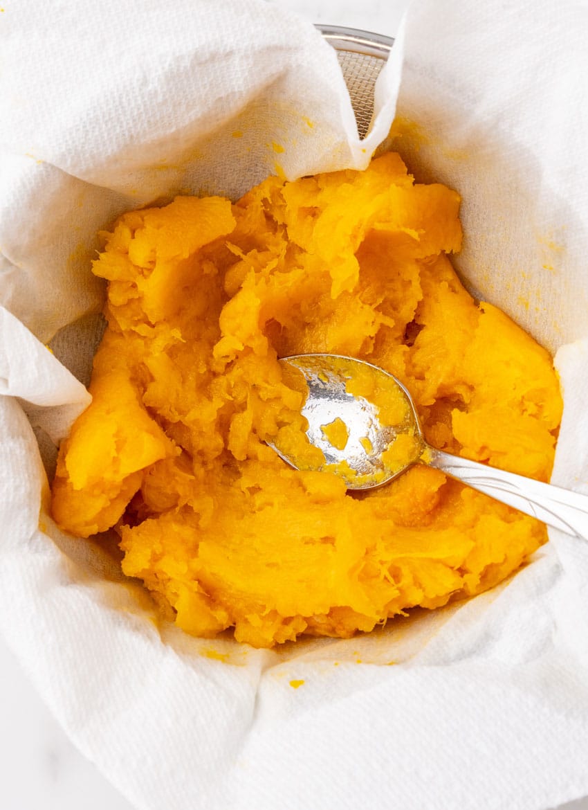 baked pumpkin being pressed through a piece of cheesecloth