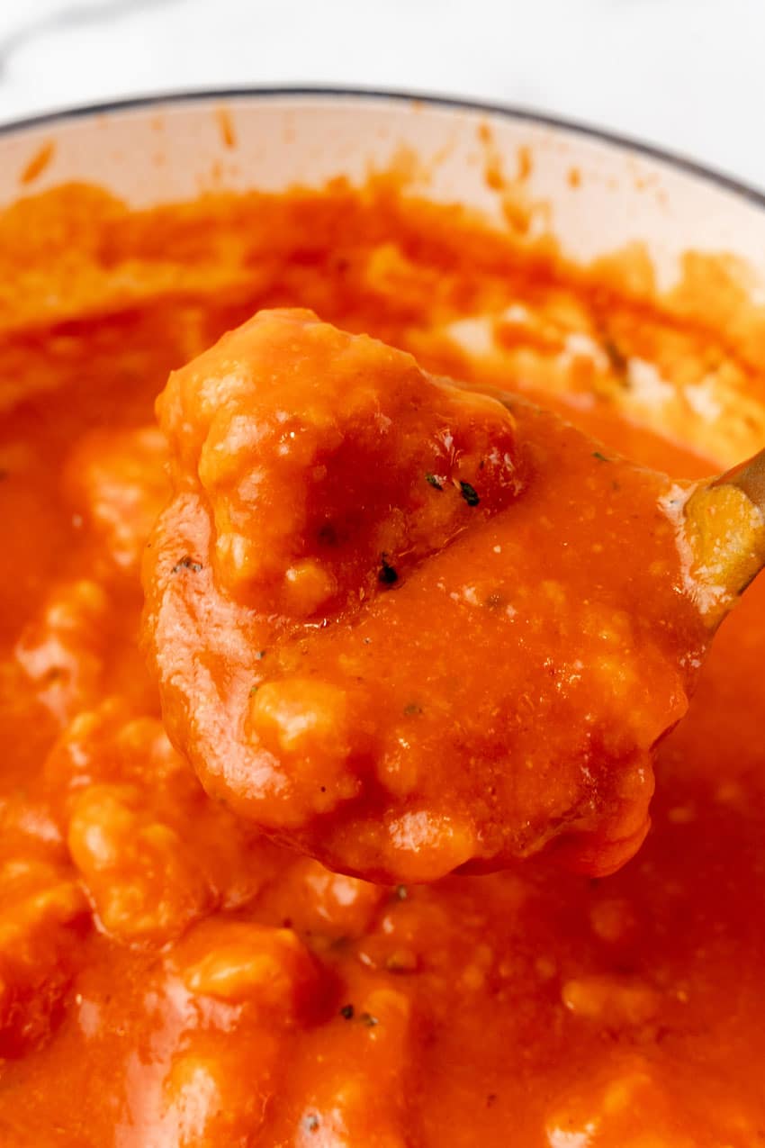 a gold ladle holding up a tomato soup covered cheddar bay dumpling