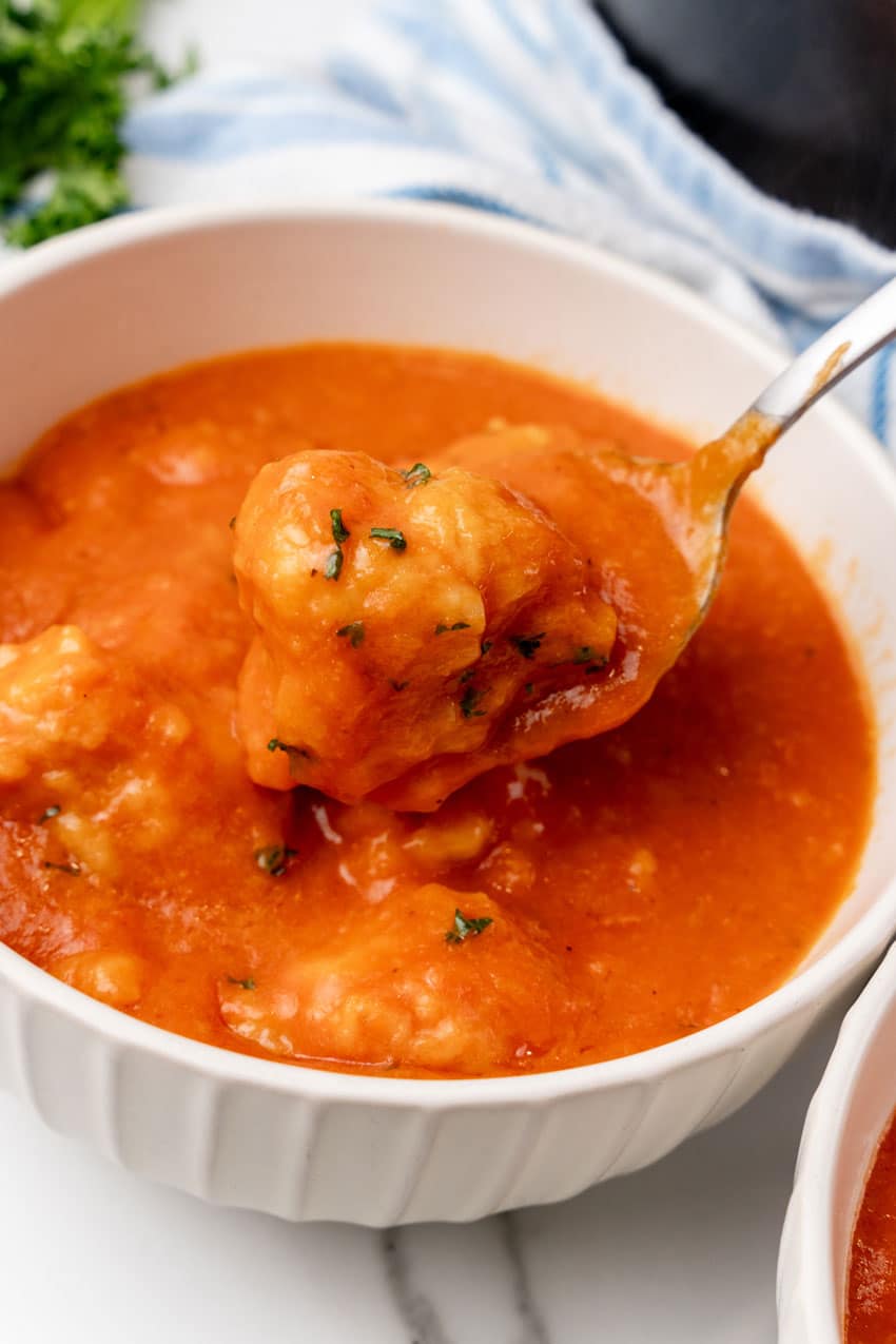 a golden spoon holding up a tomato soup covered cheddar bay dumpling