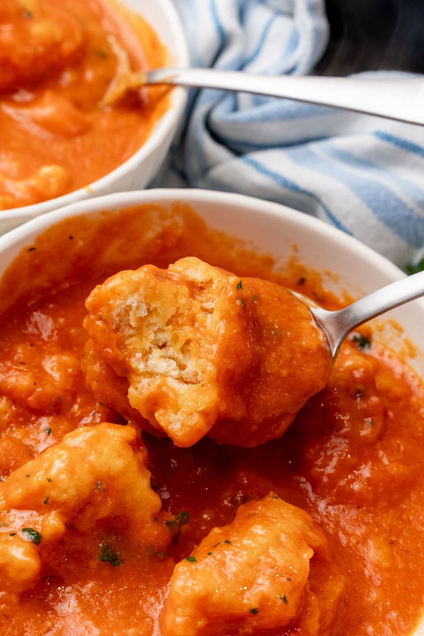 a golden spoon holding up a tomato soup covered cheddar bay dumpling