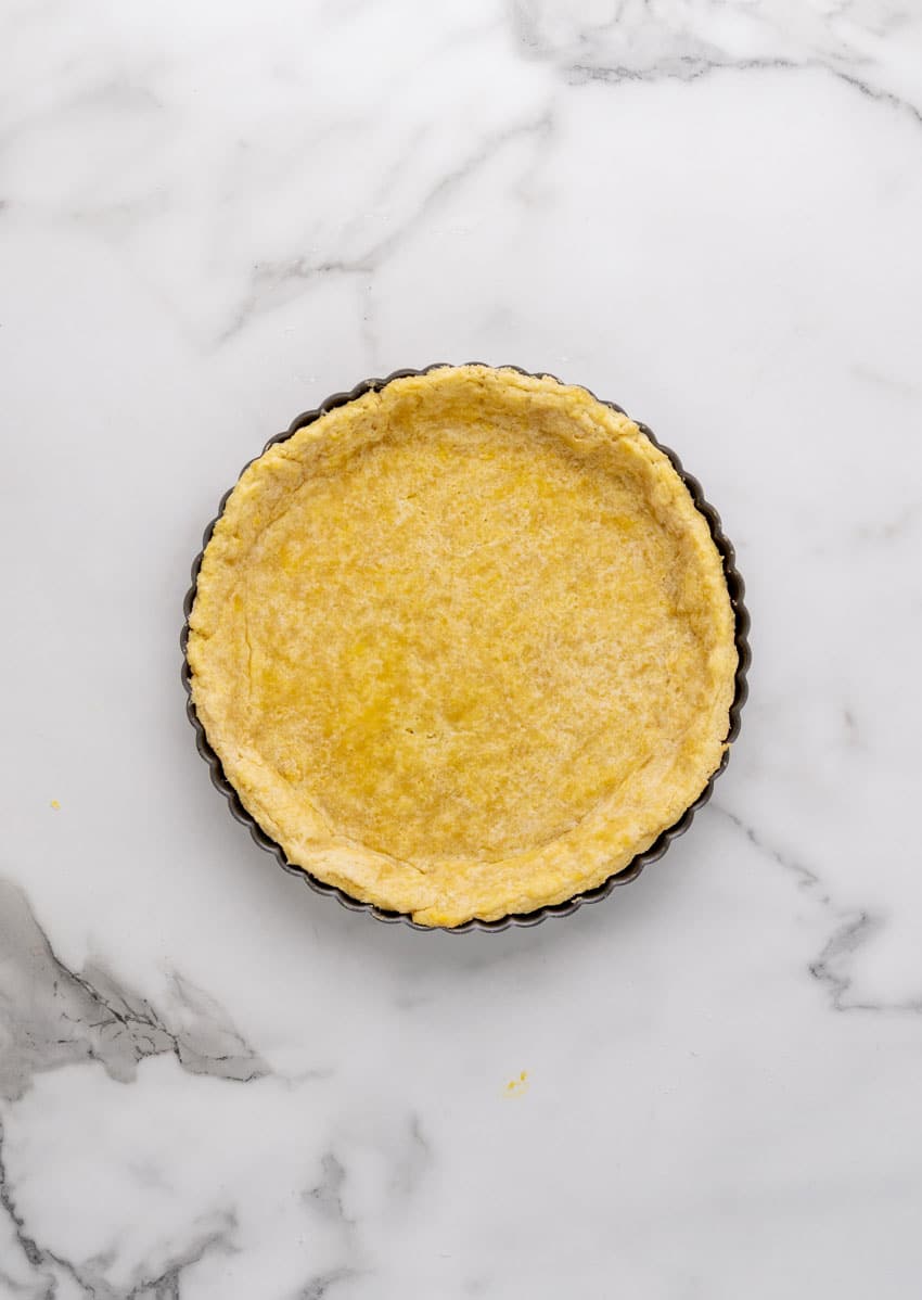 a baked tart crust in a tart pan resting on a marble countertop