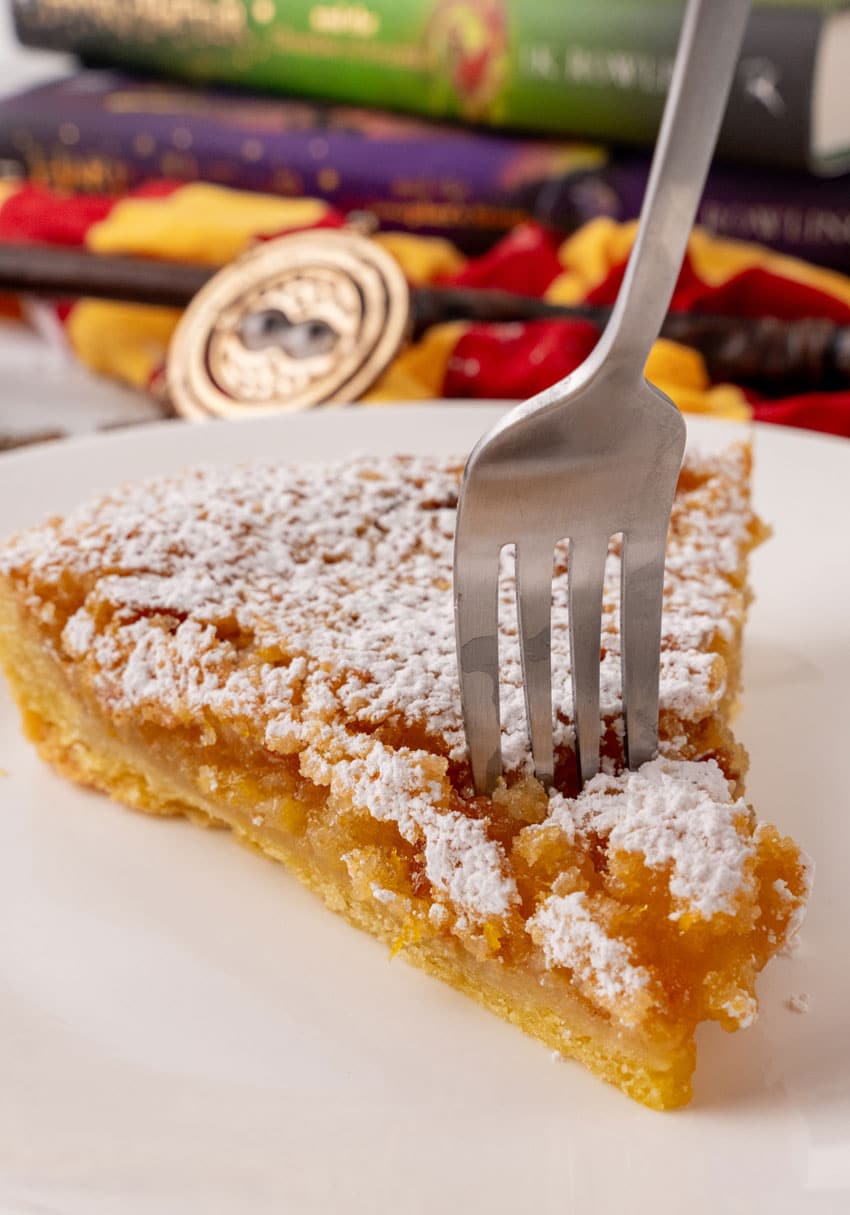 a fork digging into a slice of a harry potter treacle tart on a white plate