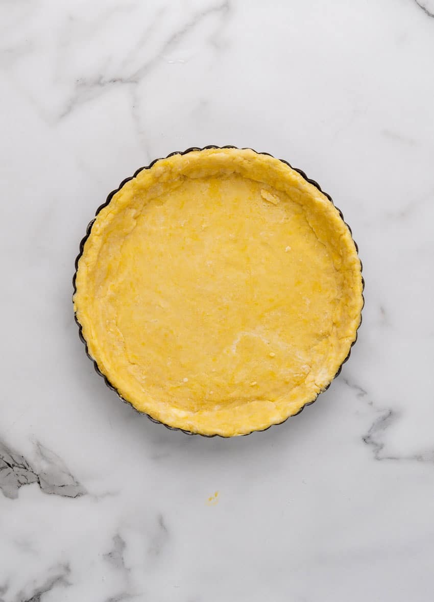 a homemade tart crust in a tart pan on a marble counter
