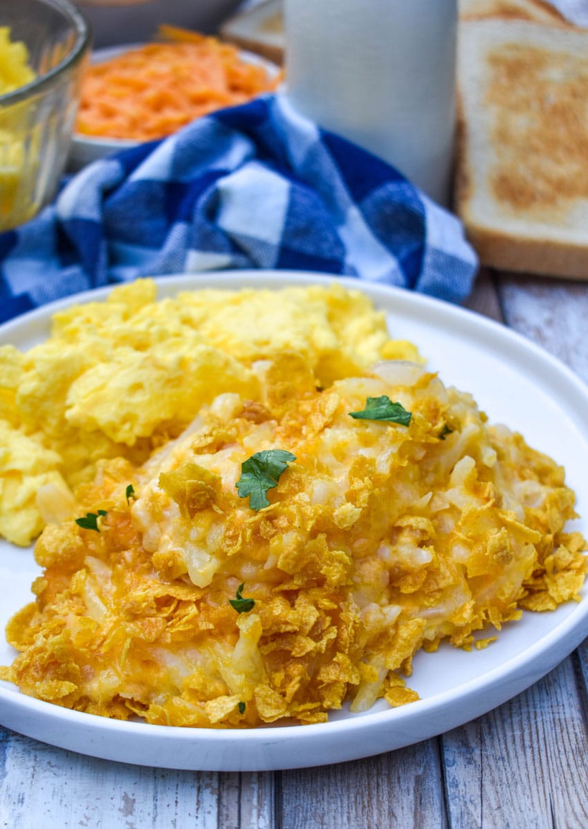 cheesy hashbrown casserole next to scrambled eggs on a white plate