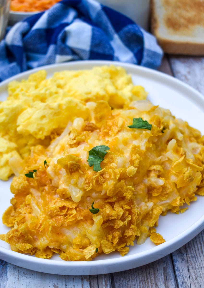 cheesy hashbrown casserole next to scrambled eggs on a white plate
