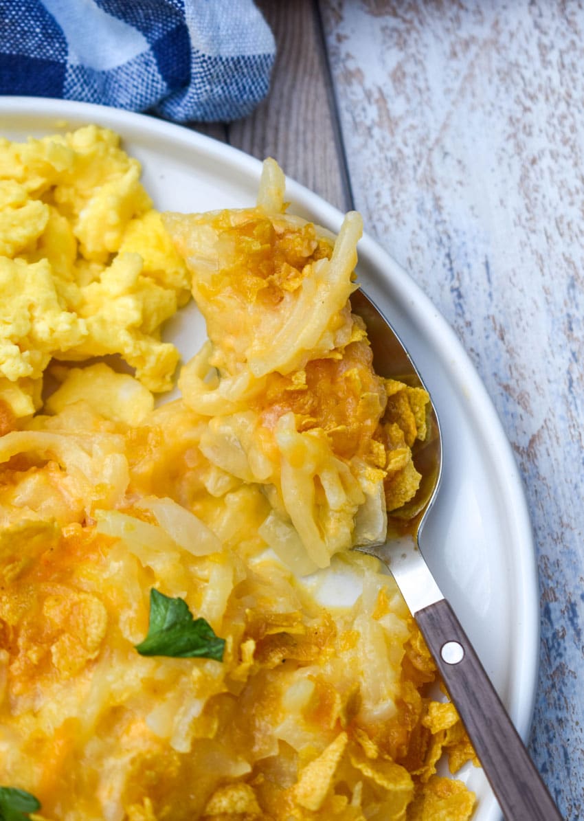 cheesy hashbrown casserole next to scrambled eggs on a white plate