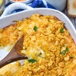 a wooden spoon scooping cheesy hashbrown casserole out of a white baking dish