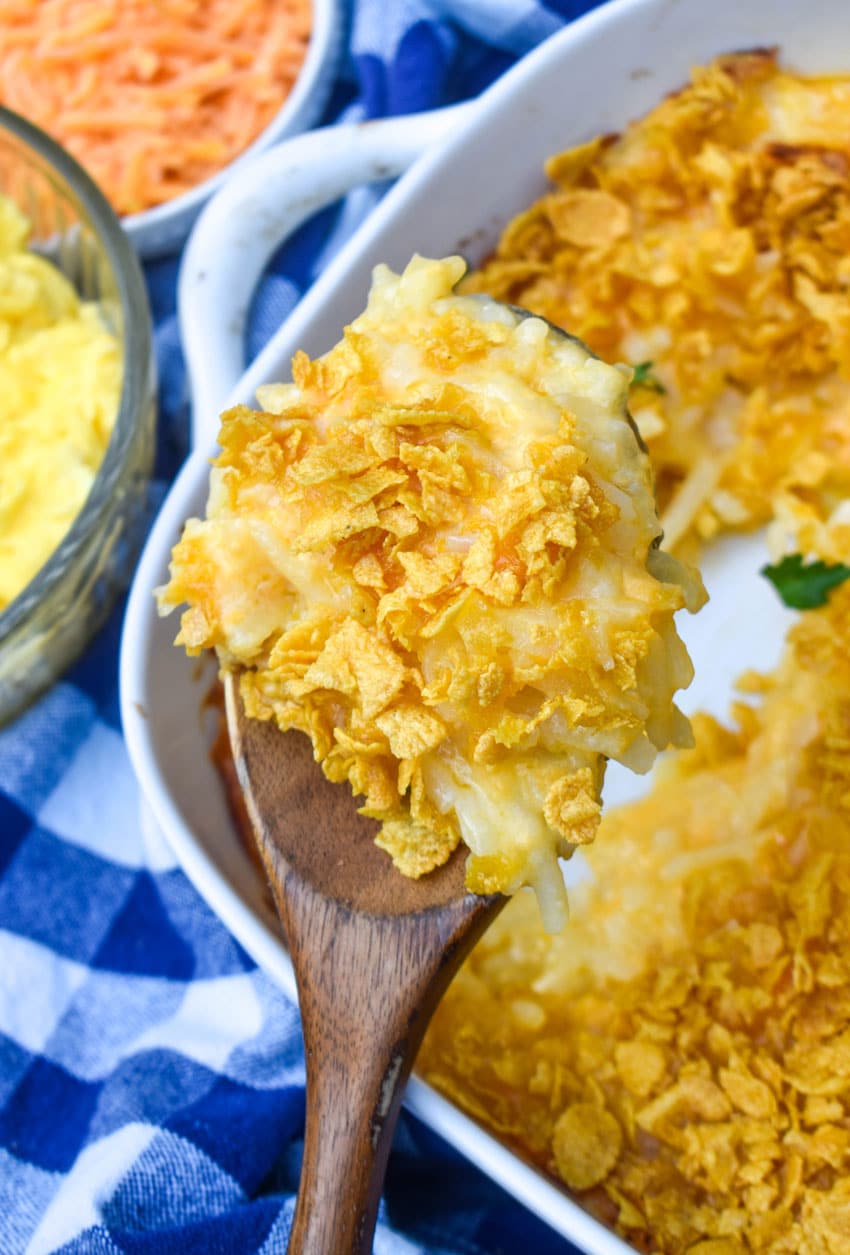 a wooden spoon holding up a scoop of cheesy hashbrown casserole