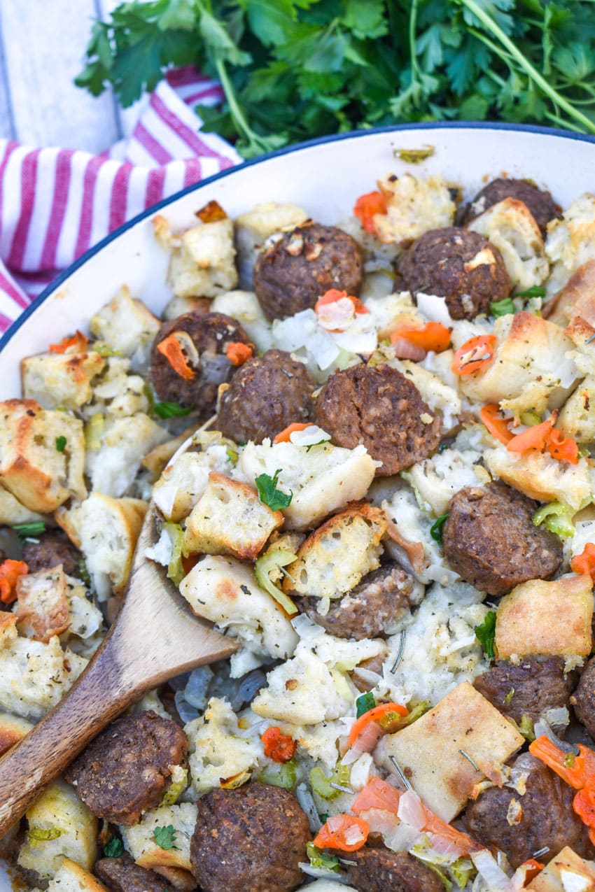 a wooden spoon scooping ciabatta meatball stuffing out of a large cast iron skillet