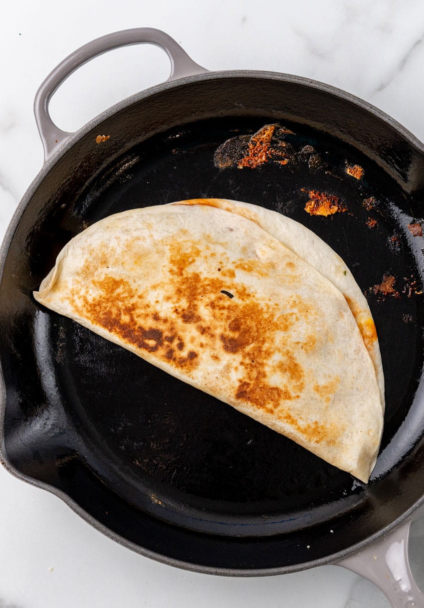 a barbecue chicken quesadilla frying in a large cast iron skillet