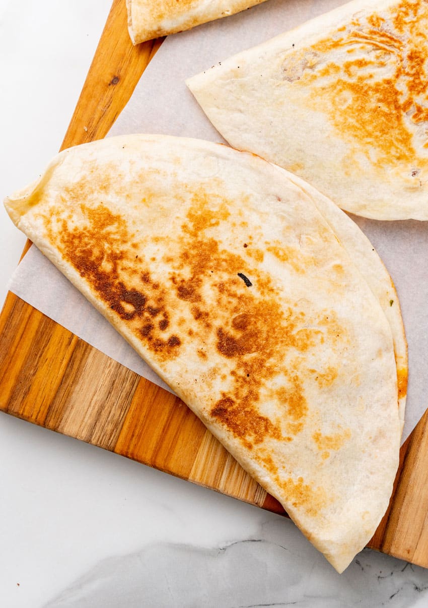 a crispy barbecue chicken and cheese quesadilla on parchment paper covered wooden cutting board