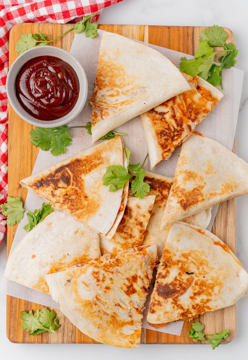 slices of barbecue chicken quesadillas on a parchment paper lined wooden cutting board