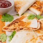 slices of barbecue chicken quesadillas on a parchment paper lined wooden cutting board