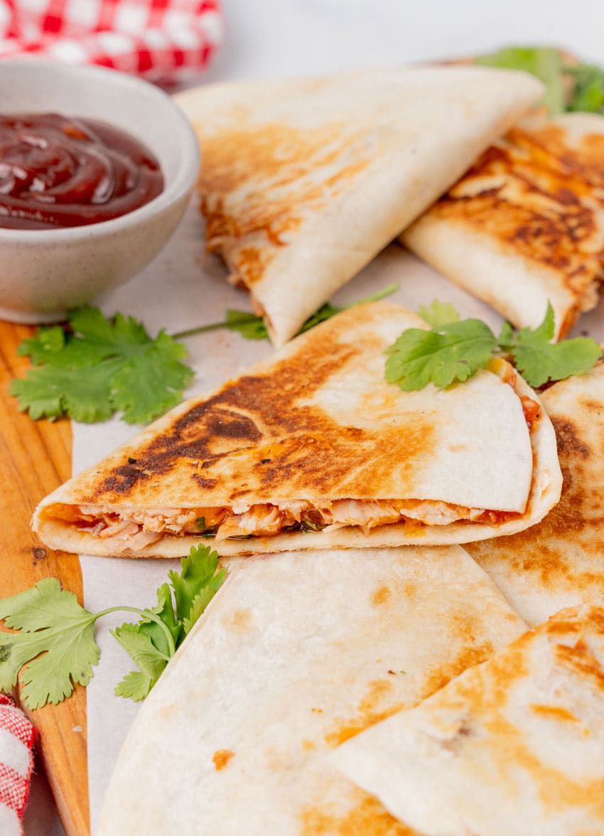 slices of barbecue chicken quesadillas on a parchment paper lined wooden cutting board