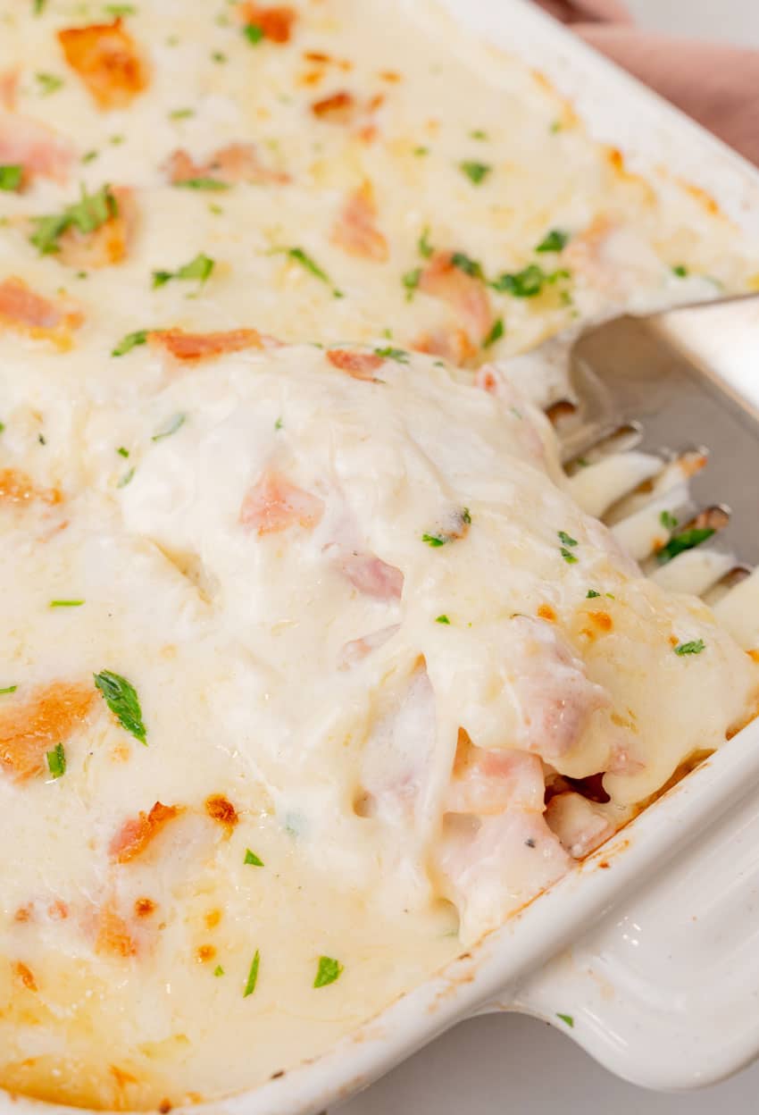 a silver spatula scooping chicken cordon bleu lasagna out of a white baking dish