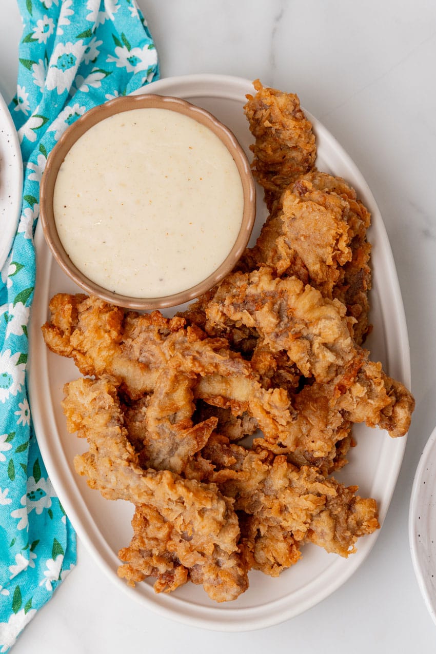 chicken fried steak fingers on a white platter with a bowl of white gravy on the side