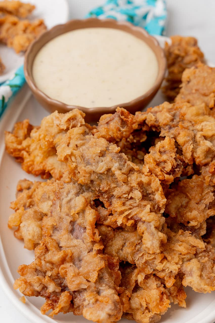 chicken fried steak fingers on a white platter with a bowl of white gravy on the side