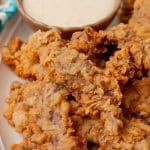 chicken fried steak fingers on a white platter with a bowl of white gravy on the side