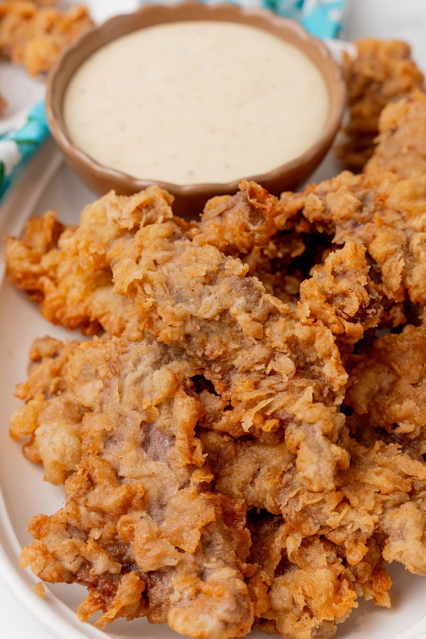 chicken fried steak fingers on a white platter with a bowl of white gravy on the side