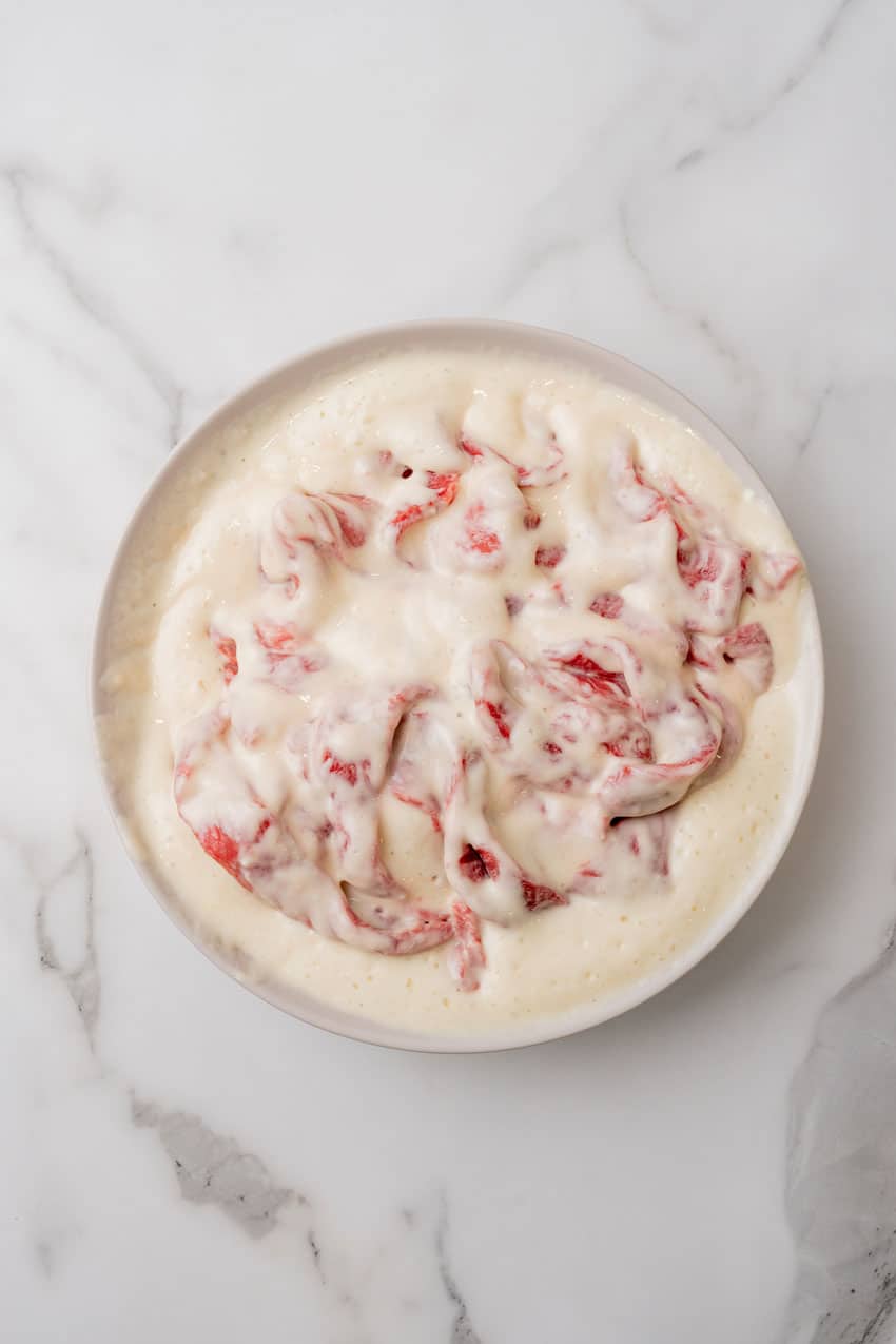 strips of cubed steak soaking in buttermilk in a shallow bowl