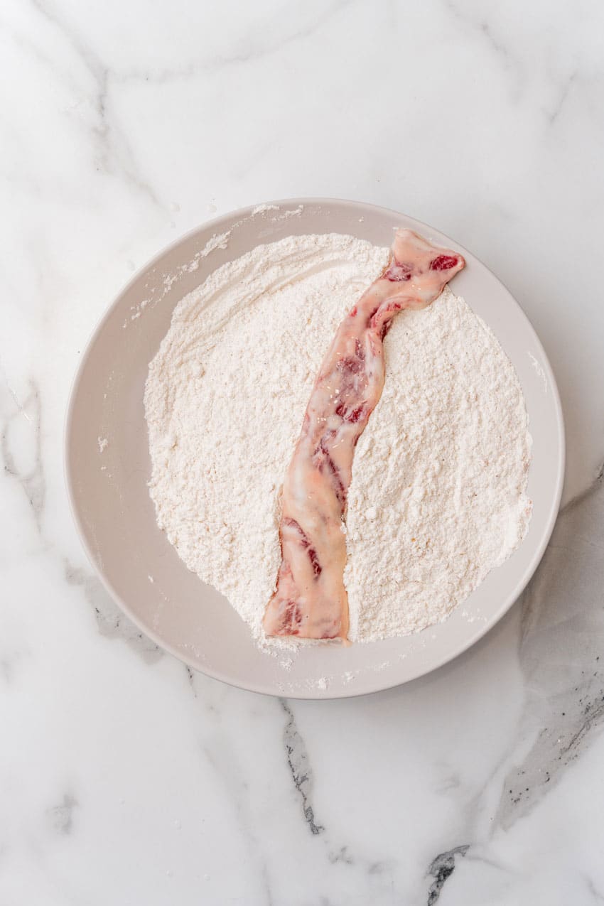 marinated strip of cube steak in flour in a shallow bowl