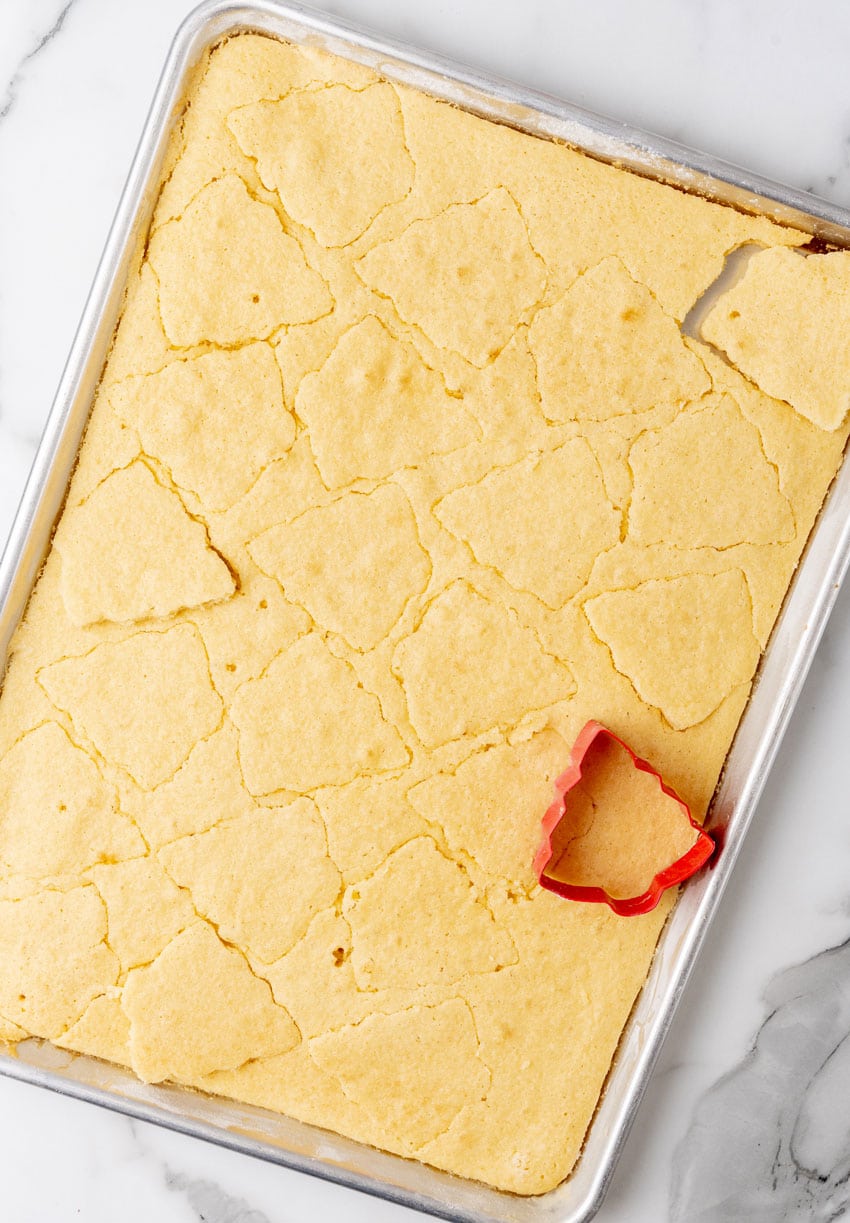 a small tree shaped cookie cutter cutting shapes out of a baked yellow sheet cake