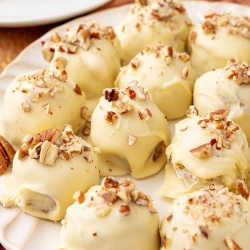 homemade pecan pie truffles covered in white chocolate on a white serving plate