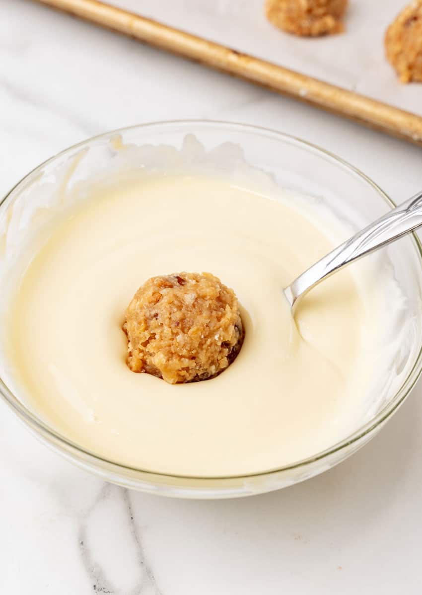 a fork dipping a pecan pie ball in melted white chocolate