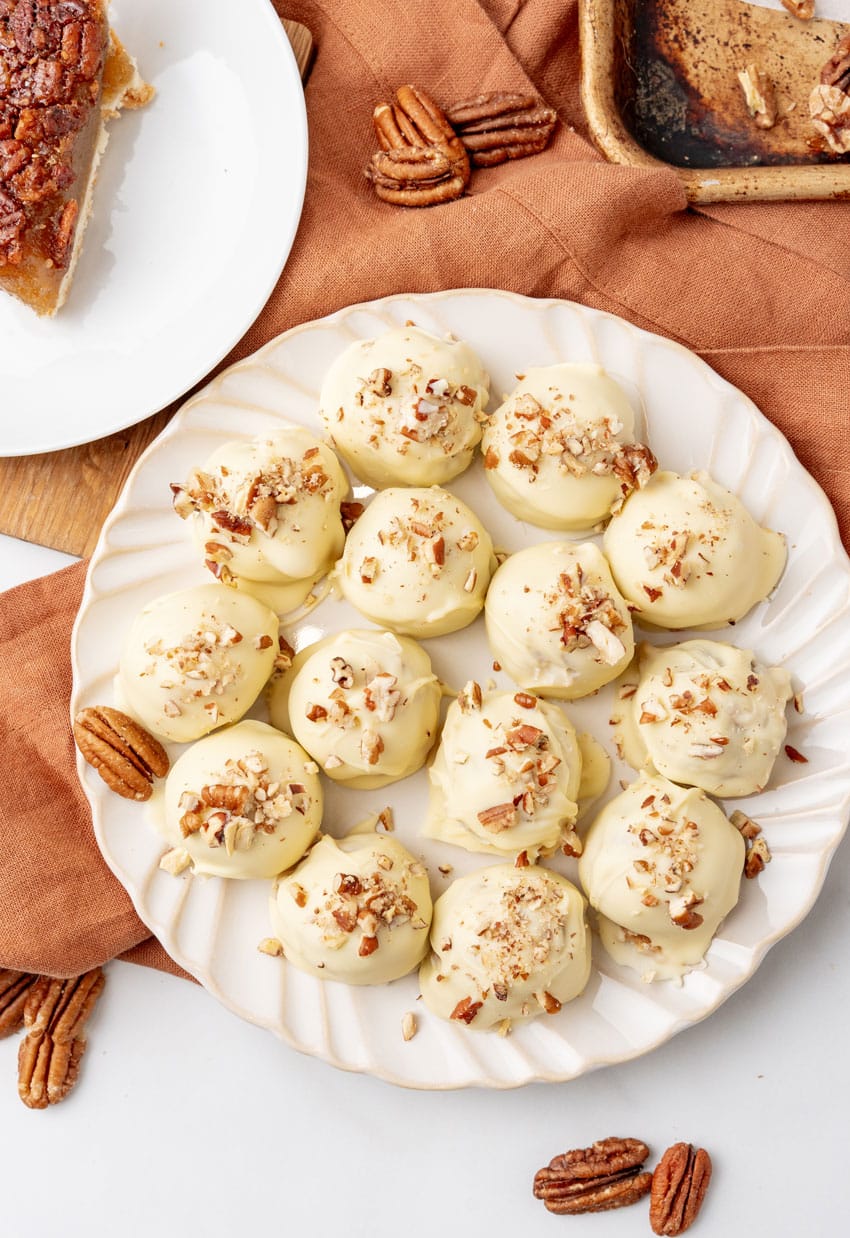 homemade pecan pie truffles covered in white chocolate on a white serving plate