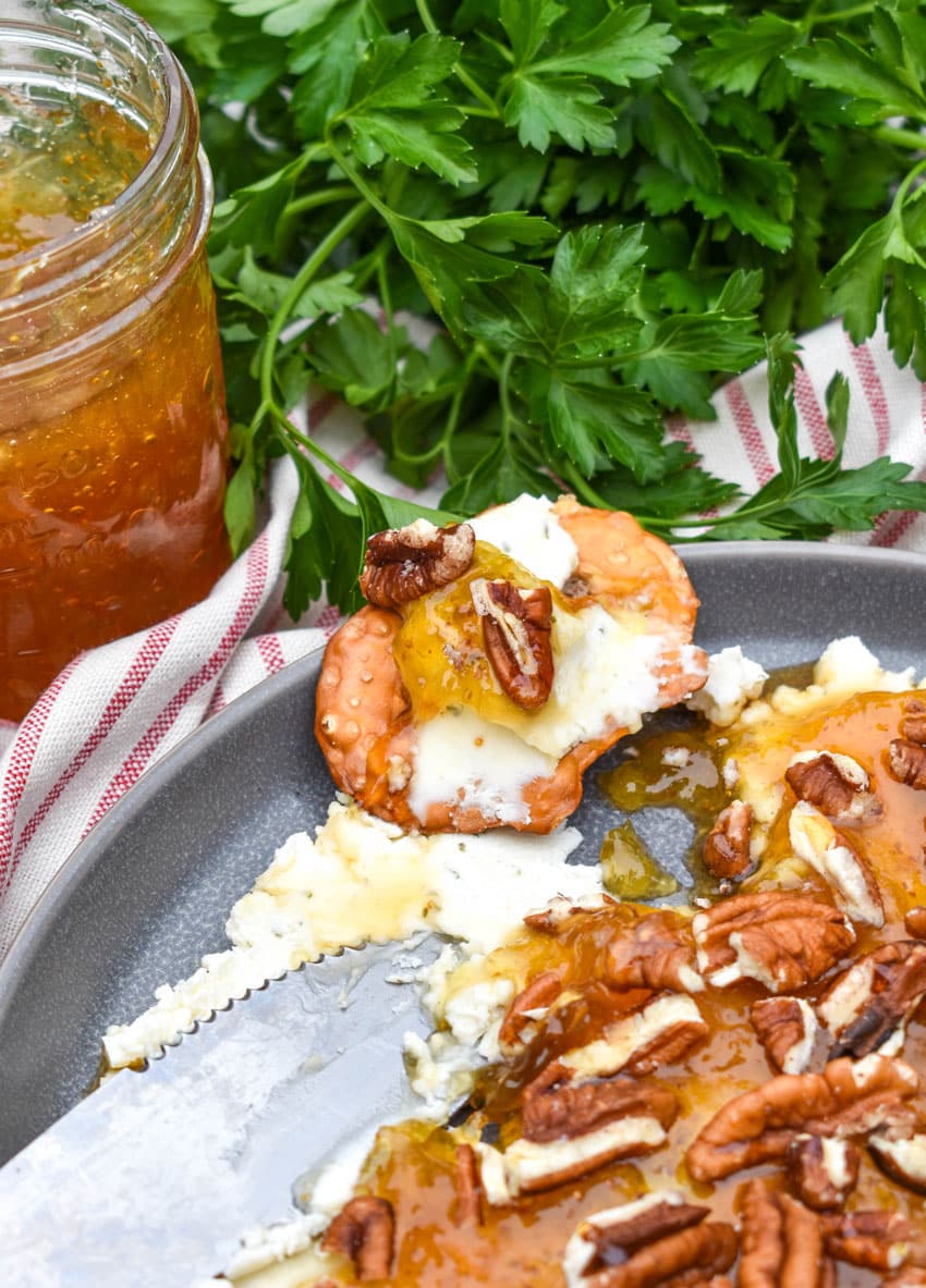 a pretzel chip topped with boursin cheese fruit spread resting on the edge of a blue plate