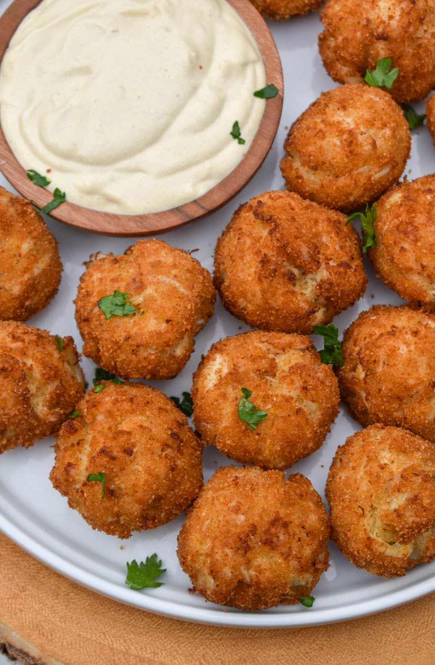 crispy crab balls on a white plate with a small bowl of creamy dip on the side