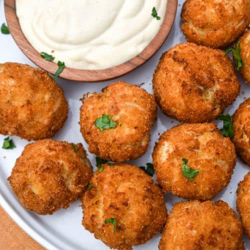crispy crab balls on a white plate with a small bowl of creamy dip on the side