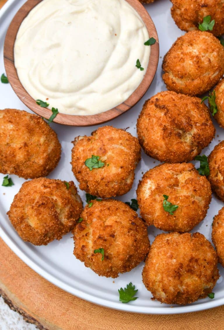 crispy crab balls on a white plate with a small bowl of creamy dip on the side