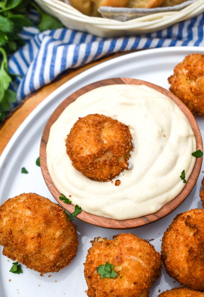 crispy crab balls on a white plate with a small bowl of creamy dip on the side
