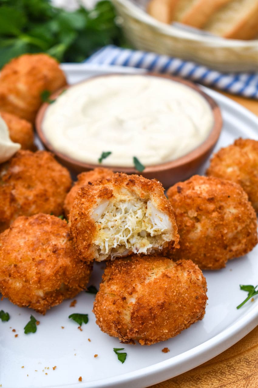 crispy crab balls on a white plate with a small bowl of creamy dip on the side