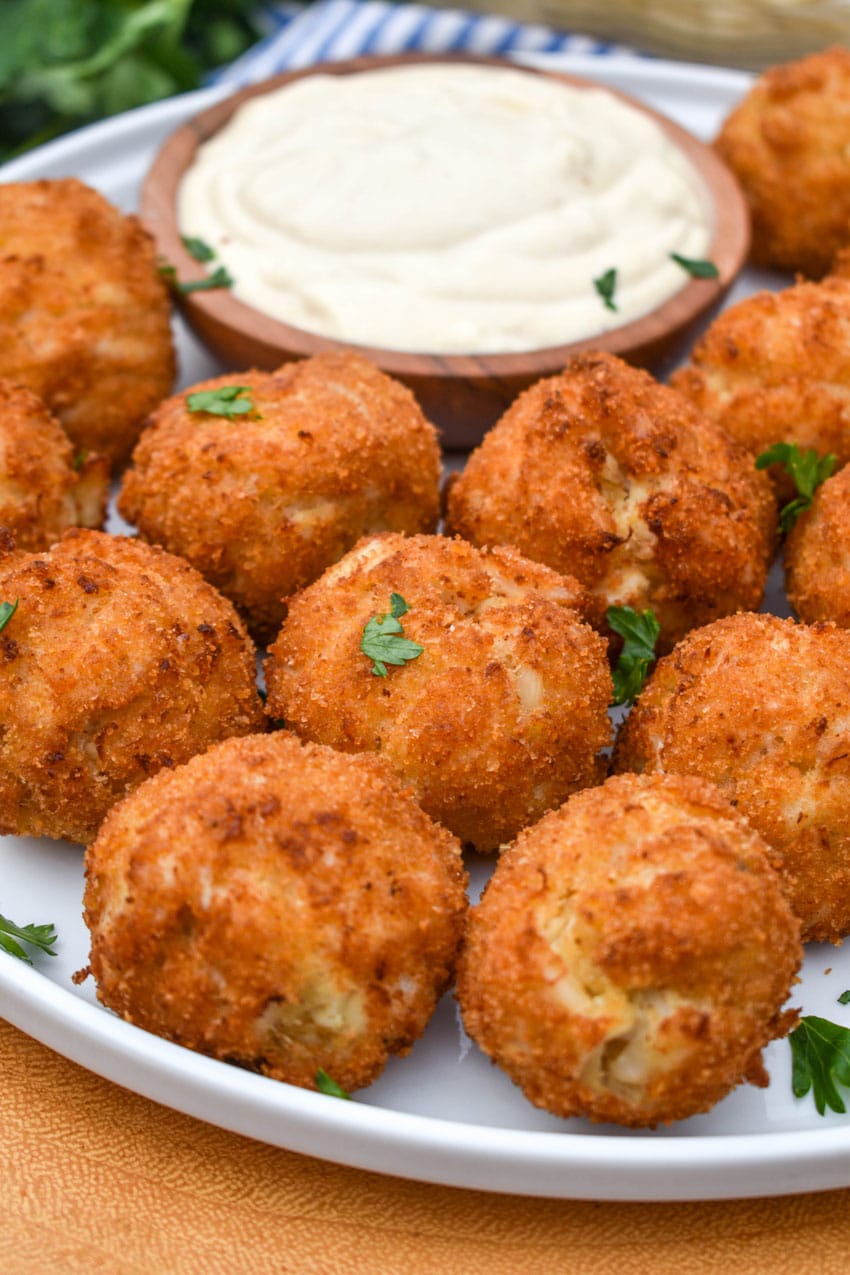 crispy crab balls on a white plate with a small bowl of creamy dip on the side