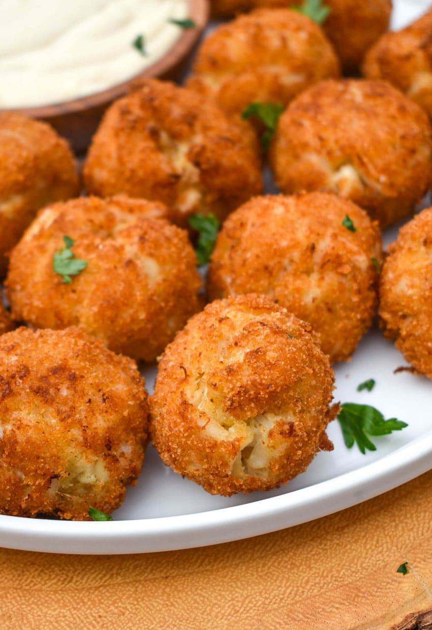 crispy crab balls on a white plate with a small bowl of creamy dip on the side